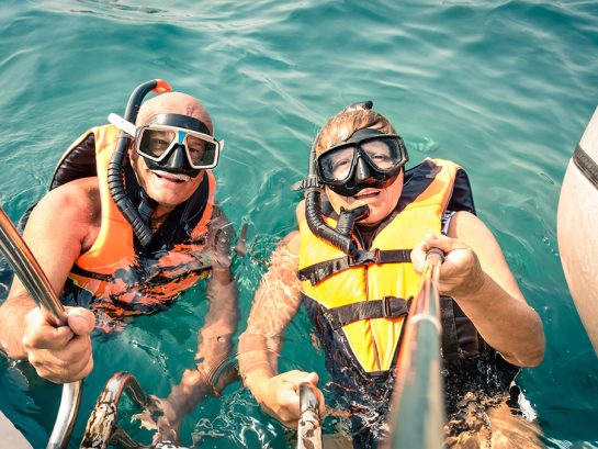 Senior happy couple using selfie stick in tropical sea excursion Senior happy couple using selfie stick in tropical sea excursion - Boat trip snorkeling in exotic scenarios - Concept of active elderly and fun around the world - Soft vintage filtered look